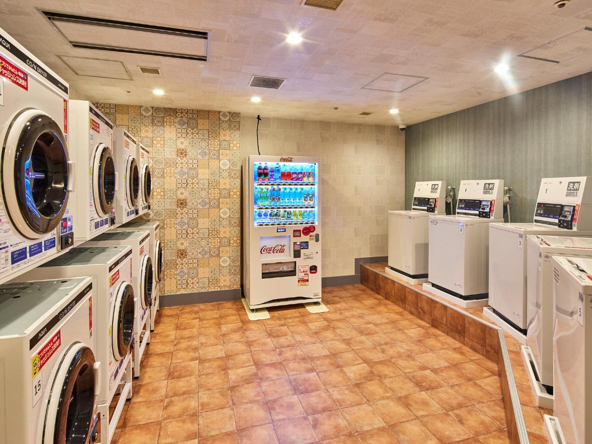 แกรนด์ นิกโกะ โตเกียว เบย์ ไมฮามะ Hotel Urayasu ภายนอก รูปภาพ The photo shows a laundry room equipped with several washing machines and dryers. On the left side, there are multiple front-loading washing machines arranged in a row, and on the right side, there are dryers. In the center, there is a vending machin